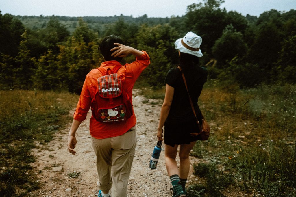 Two women walking at Forks of the Credit Provincial Park. One woman is wearing a red Hello Kitty backpack, and the other is wearing a white hat