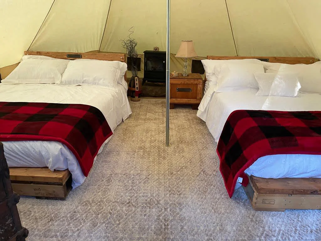 Interior of Sibo's Bell Tent in Verona, Ontario with two double beds, a heater, a bedside table and lamp