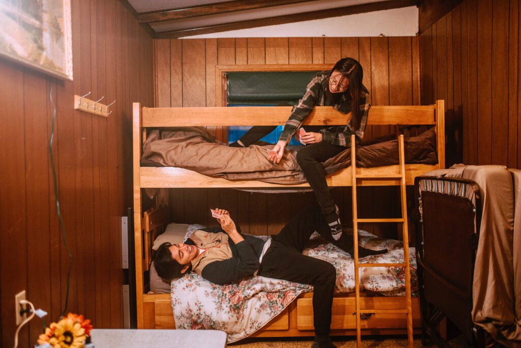 Angelo and Maria from SYDE Road on the top bunk enjoying some card games in the rustic cozy cabin in Minden, Ontario - Hipcamp Canada Listing