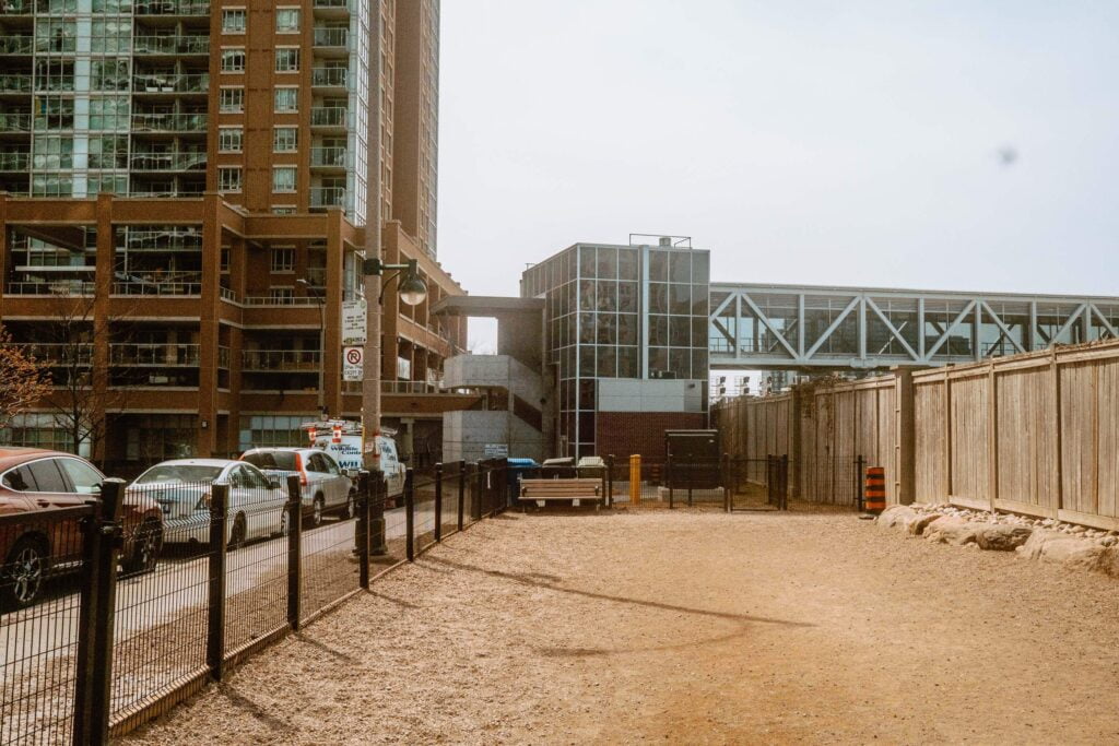 Image of the West end of Bill Johnston Dog Park - Liberty Village Dog Park. Street Parking signage and cars are parked to the side of the dog park