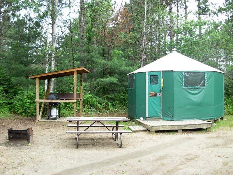 A green provincial park yurt with a picnic table and a sheltered BBQ area